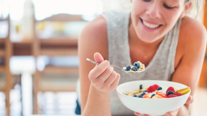 A woman eats a bowl of oatmeal with berries