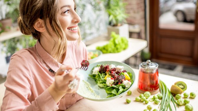 A woman smiles while eating a salad after figuring out the differences between emotional eating vs binge eating