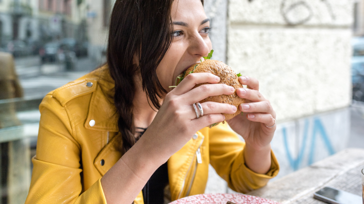 A woman eats a burger while practicing intuitive eating